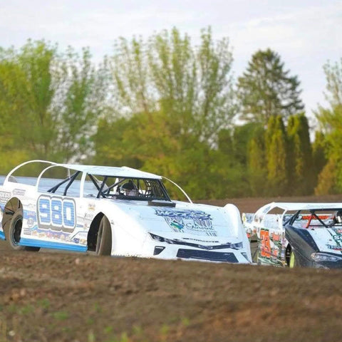 Race cars on dirt track in outdoor setting with trees in background