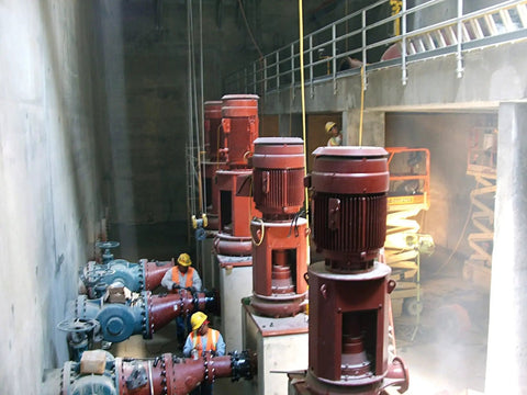 Industrial pumps and workers in a concrete facility with large red motors and pipes.