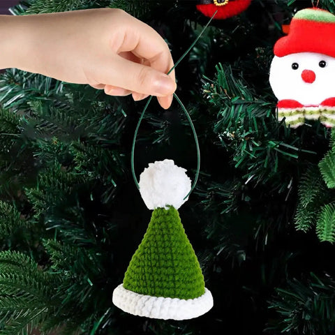 Hand holding green and white knit hat ornament hanging on a Christmas tree