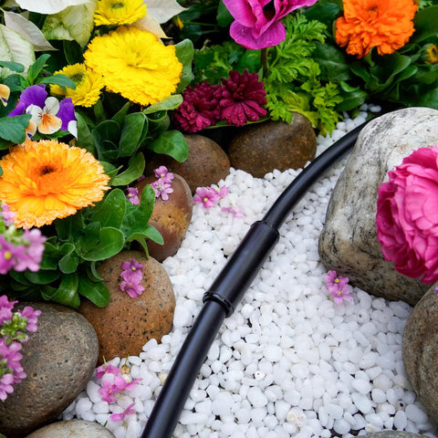 1/2-inch compression coupling on black poly drip irrigation tubing in a garden bed with white decorative gravel and colorful flowers