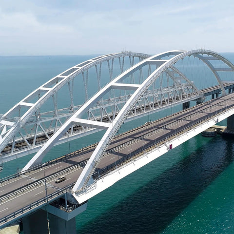 White arched road bridge over turquoise water with roadway and steel truss supports.