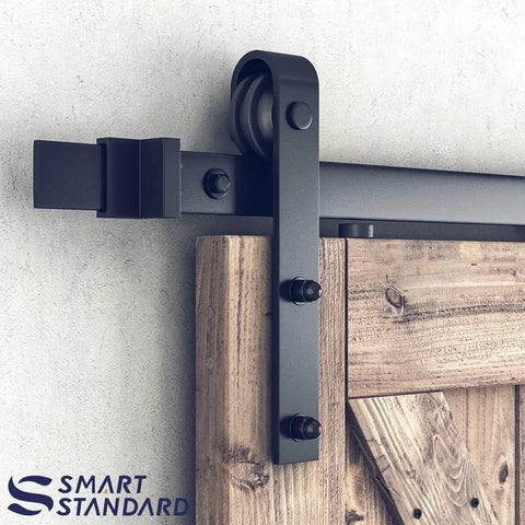 Six Foot Double Barn Door Hardware Kit For Home Use Sliding Door Track That Glides Smooth And Quiet DIY Friendly Install Fits An 18 Inch Wide Door Panel J Shape Hanger Black Finish close-up view of metal hardware on wooden door.
