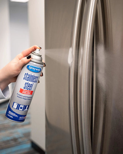 Sprayway stainless steel cleaner aerosol can held in hand, spraying onto a stainless refrigerator door.