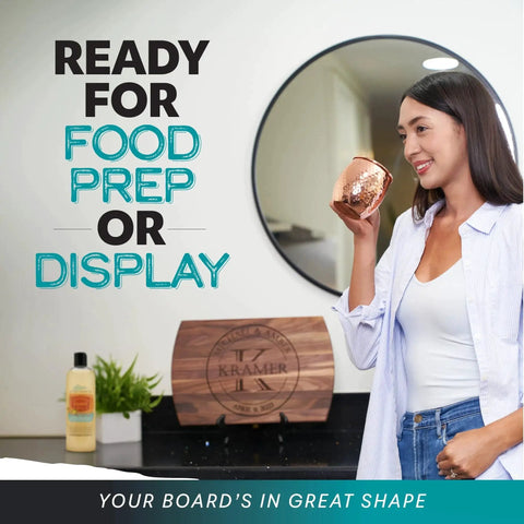 Woman holding cup near a Personalized Wood Cutting Board With Gift Box, Stand, And Oil Included For Weddings, Anniversaries, Birthdays Or Mothers Day, Laser Engraved And Custom Engraved In Cherry, Maple, Or Walnut For Her By Blue Ridge Mountain Gifts displayed on a counter.