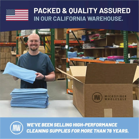Man holding blue microfiber cloth for packaging at California warehouse with stacks of microfiber towels on table.