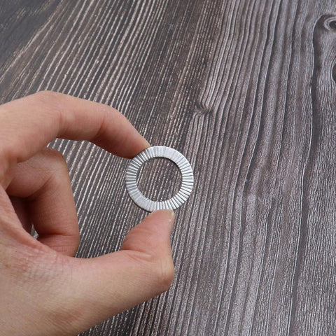 Close-up of a silver manganese steel wedge lock washer held between fingers.
