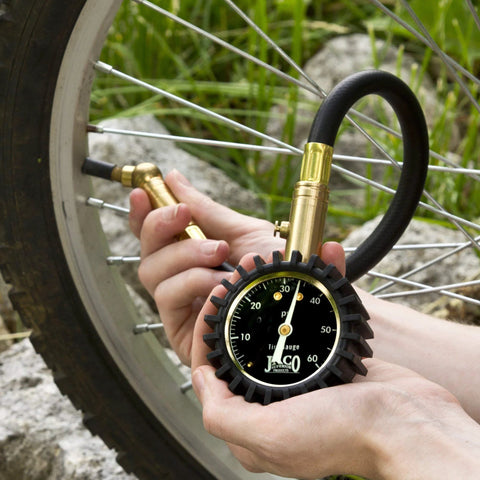 JACO ElitePro tire pressure gauge with brass body and black protective guard, measuring up to 60 PSI on a bicycle tire valve