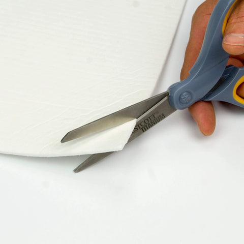 Lynn Manufacturing high-temperature gasket paper sheet, white 1/8 in thick, being cut with scissors.