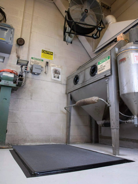 Industrial workspace with machinery, fan overhead, and caution signs on walls.