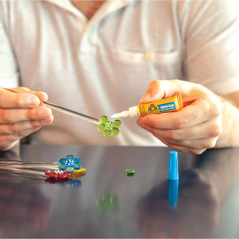 Person using Clear All Purpose Glue In Four 3 Gram Tubes With Fast Setting for Projects and Repairs on a craft project with colored beads.