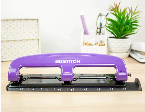 EZ Squeeze Reduced Effort 3 Hole Punch for busy office, purple finish, showing integrated ruler and durable metal construction on desk