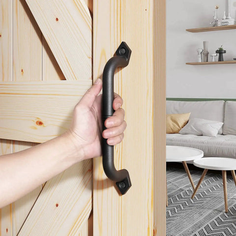 Hand holding 10 Inch Barn Door Pull Handle And Gate Handle in Rustic Black Aluminum, ergonomic chamfered edges, installed on wooden door