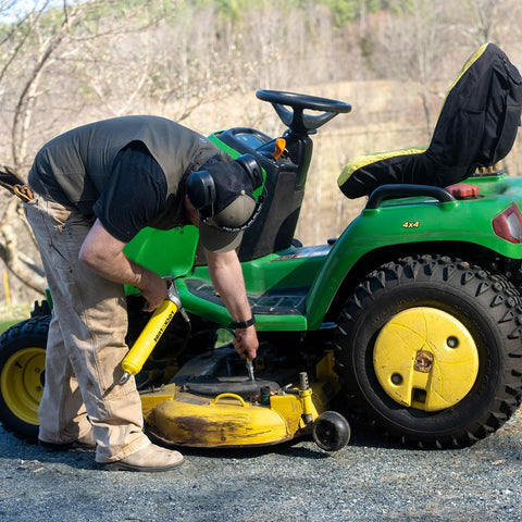 LockNLube Premium Pistol-Grip Grease Gun in use by a worker beside a green riding lawn mower; yellow tool visible.