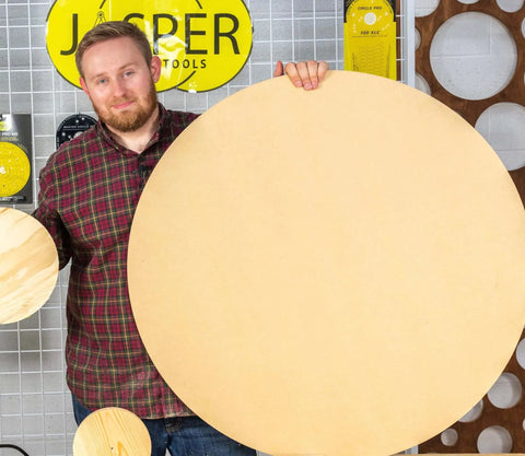 Man holding large wooden disc made with Blemish Free Pivot Plate For Circle Cutting No Center Hole Required For Flawless Discs And Tabletops Clean Edges Easy Router Jig Accessory Works With All Circle Cut Guides For Top Notch Results, standing in workshop with Jasper Tools background.