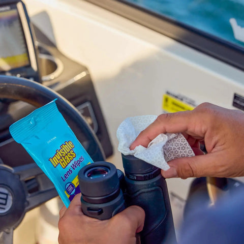 Cleaning binoculars with Streak Free Lens Cleaning Wipes For Glasses Cameras Binoculars 16 Count on a boat, showing wipe in use.