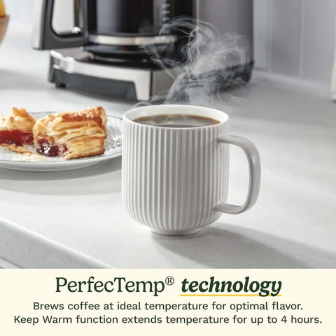 14 Cup PerfecTemp Programmable Coffee Maker With Glass Carafe And 1 4 Cup Setting Brew Strength Control Brew Pause And Over Ice Function In Black Stainless Steel on counter behind steaming mug and pastry