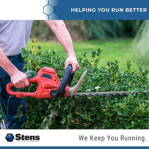 Person using red electric hedge trimmer on green bushes outdoors.