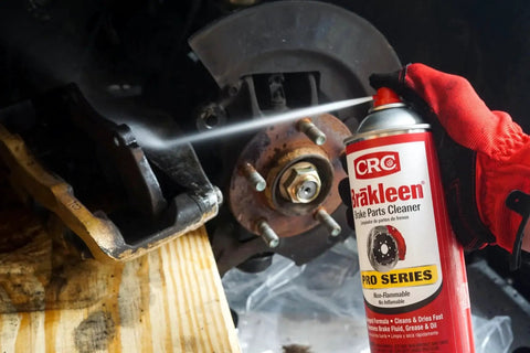 CRC Brakleen brake parts cleaner spray used on rusty brake rotor and hub, red-gloved hand