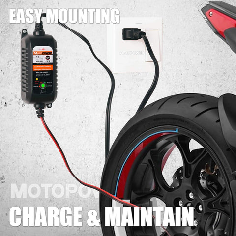 All Weather 12V Battery Charger Maintainer And Desulfator With Automatic Trickle Charge For Cars Boats And Powersports 800mA Lead Acid AGM Gel Cell Ready By MOTOPOWER MP00205A mounted on wall with motorcycle tire in view.