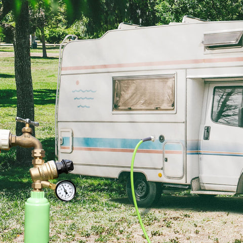 Brass RV water pressure regulator with gauge and inlet screen, adjustable knob, connected to RV water hose.