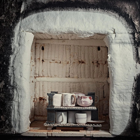 White ceramic fiber insulation blanket lining kiln interior with a two-tier shelf holding ceramic mugs