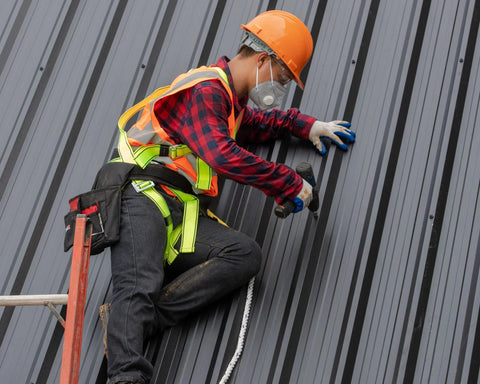 BCP Fasteners construction scene: worker on metal roof wearing orange hard hat, neon safety vest, gloves