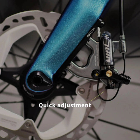 Juin F1 hybrid hydraulic disc brake caliper installed on blue bicycle frame near rotor (side view).