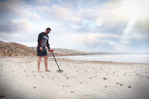 Person using Vanquish 440 Multi Frequency Metal Detector With Multi IQ Technology on a sandy beach under a cloudy sky.
