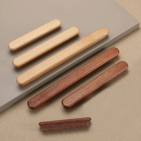 Two sets of long, slim wooden drawer handles in light and dark wood tones, laid out on a beige surface, showcasing minimalist design.
