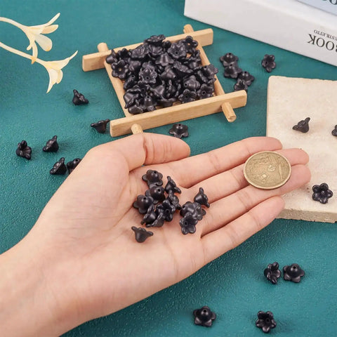 Black Acrylic Flower Bead Caps 100 Pcs Five Petal Frosted Resin Flower Spacers in hand on green surface