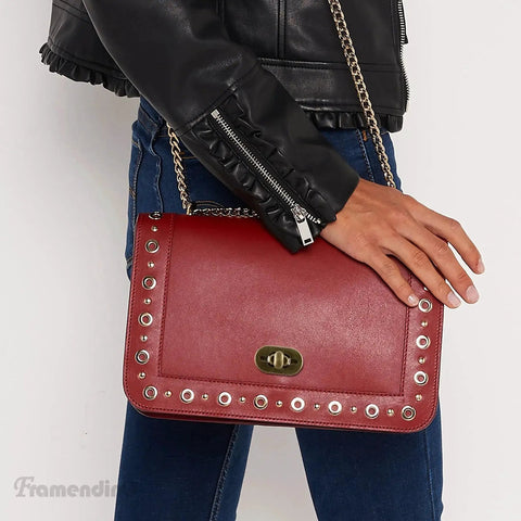 Person holding bag with antique bronze twist lock clasp, detail view of purse closure hardware and decorative studs.