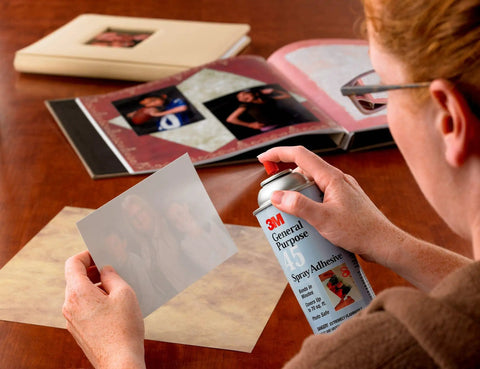 Person using a spray adhesive to attach a photo to a scrapbook, Hi-Strength Spray Adhesive 90, Low VOC 14.6 oz can visible.