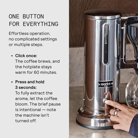 Person operating the Aarke coffee maker with stainless steel build, featuring a single-button control for brewing and warming.