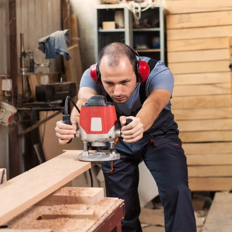 Carpenter using a handheld router in a workshop, fitting Brass Router Template Guides Bushing Set for precise woodwork.