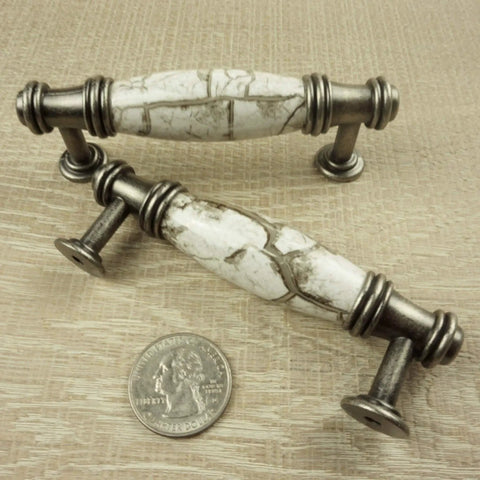 Two ornate silver gray cabinet pulls with marbled white accents, shown with a coin for scale.