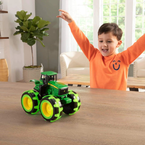 John Deere Monster Treads Lightning Wheels Monster Truck Toy With Motion Activated Lights, Oversized Monster Truck Wheels, Durable Build For Rollover Fun, Realistic Tractor Look For Ages 3 Years And Up on table with child in background