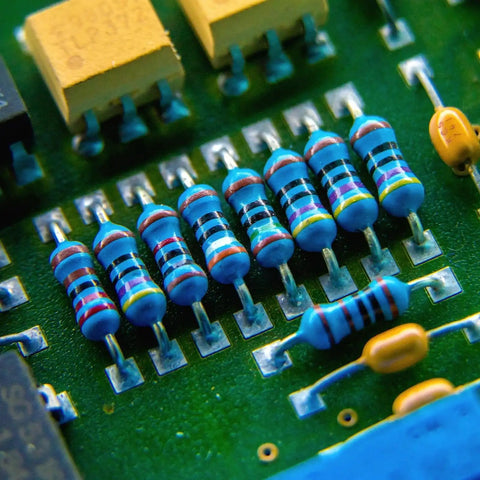 Close-up of blue axial metal-film resistors with color bands mounted on a green PCB