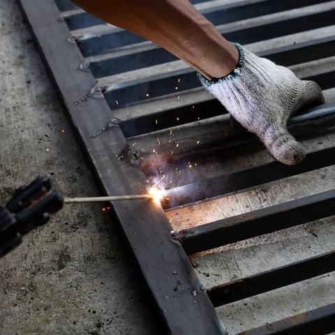Person welding a metal grate, sparks flying, wearing protective glove