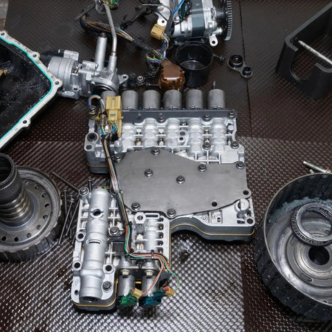Automotive transmission components on workshop floor with assorted gears and parts, focus on metal assembly, no rings visible