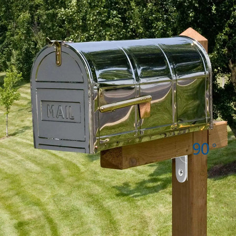 Stainless steel mailbox mounted on wooden post in a grassy yard with trees in the background.