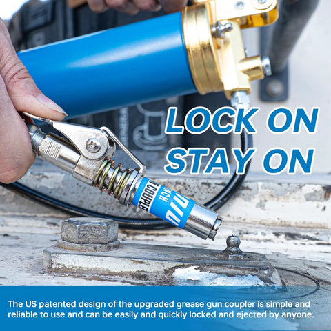 Grease gun coupler with spring-loaded locking lever; silver metal, 1/8" NPT fitting, blue grease gun visible in background.