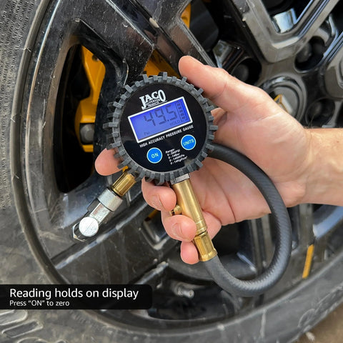 JACO ElitePro digital tire pressure gauge with blue backlit display held to a vehicle tire; reads 49.5 psi.