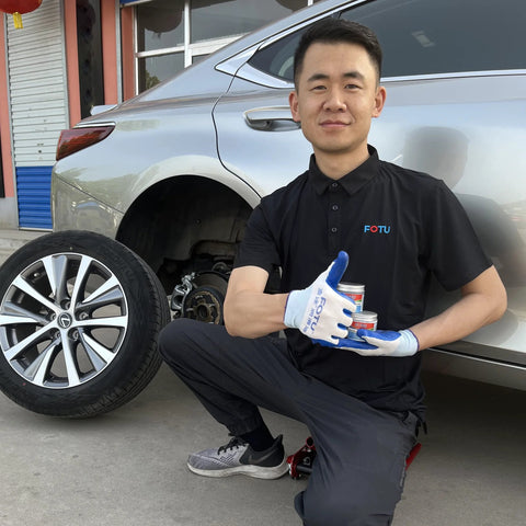 FOTU brake caliper grease cans (two) held by mechanic beside a silver car.