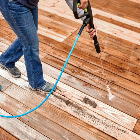 Pressure washer nozzle tips set with 1/4 in quick-connect, attached to spray wand and blue hose, cleaning a wooden deck.