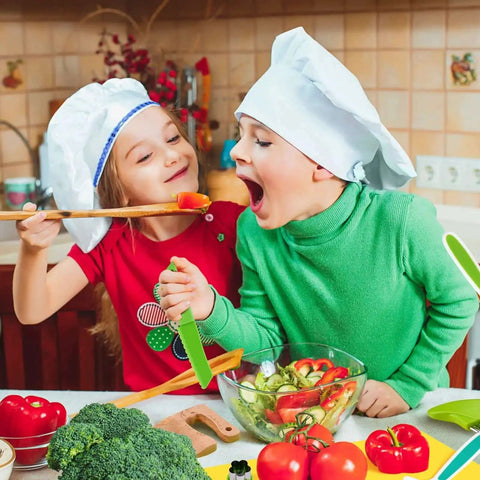 Two children in chef hats using Real Kitchen Skills For Little Chefs 13 Piece Toddler Knife Set with vegetables on the counter.