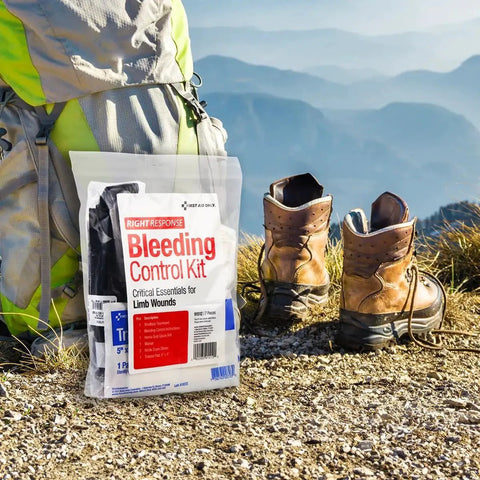 Bleeding Control Kit For Limb Wounds With Tourniquet 7 Pieces Portable First Aid Set next to hiking boots on a mountain trail