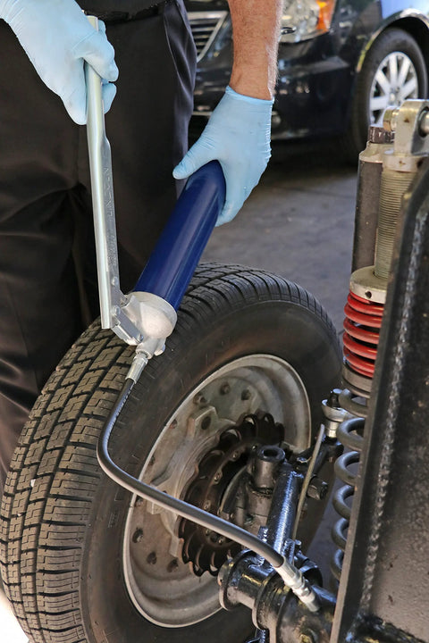 Lincoln 1147 lever-action grease gun with 18-inch hose used on a car suspension near a tire.