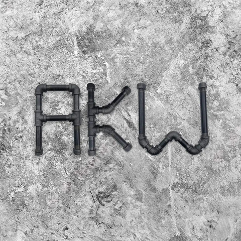 Metal pipes arranged to form the letters 'AKW' on a textured stone background.