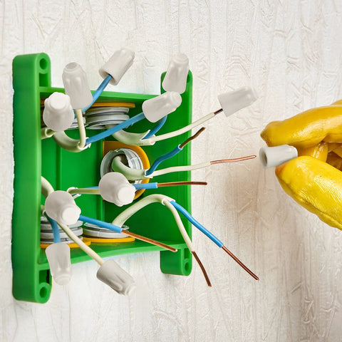 Ceramic wire connectors in a green junction box; white twist caps on blue and white wires, gloved hand holding one
