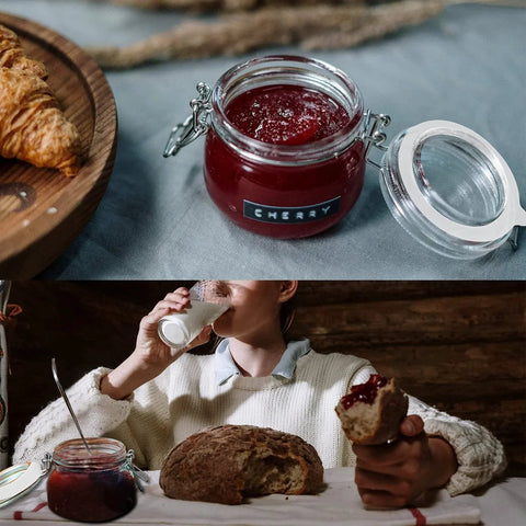 Open mason jar of cherry jam next to croissant, person holding bread with jam inside, glass of milk, cozy kitchen setting